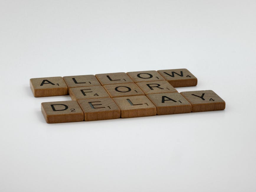 An image displays wooden Scrabble-style tiles spelling out the phrase 'ALLOW FOR DELAY' arranged on a plain white surface. The tiles include letters with black printing, and small point values are vis